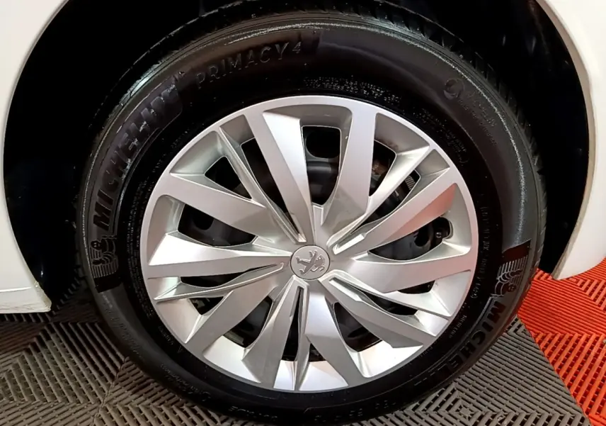 Gros plan sur la roue avant droite d'une Peugeot 208 blanche, mettant en valeur la jante alu et le pneu Michelin.