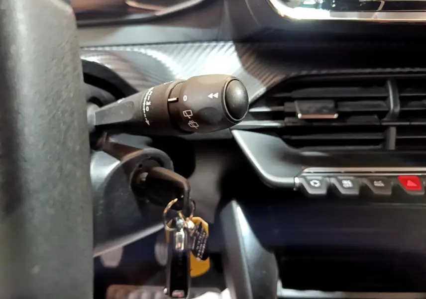 Gros plan sur la commande d’essuie-glace et la clé de contact insérée dans le tableau de bord noir de la Peugeot 208 blanche.
