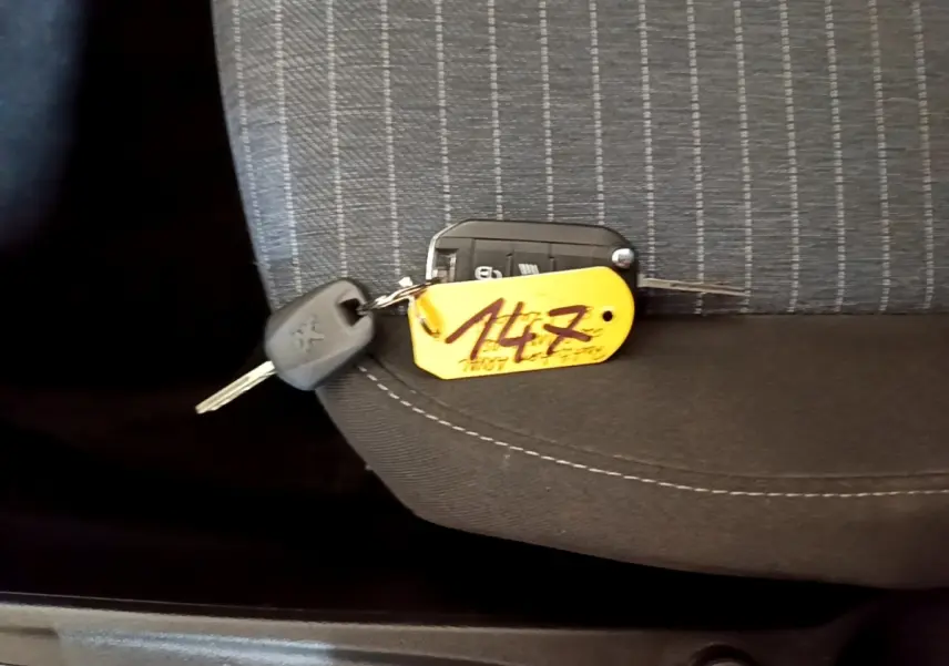 Clé de Peugeot 208 diesel 2022 posée sur un siège tissu gris à motifs, avec porte-clés jaune marqué "147".