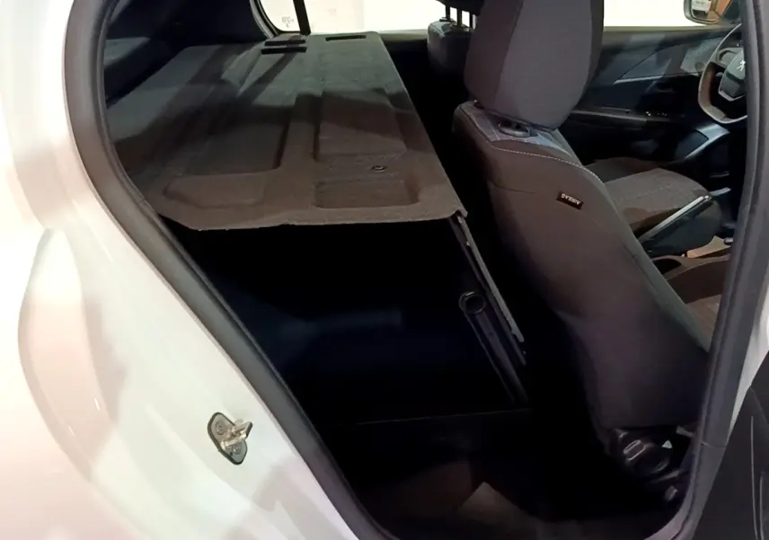 Vue intérieure côté arrière droit du coffre ouvert d'une Peugeot 208 blanche avec banquette rabattue et sièges tissu gris.