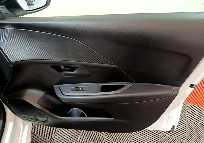 Vue rapprochée de la porte avant gauche blanche d’une Peugeot 208 2022 avec insert imitation carbone et commande de lève-vitre.