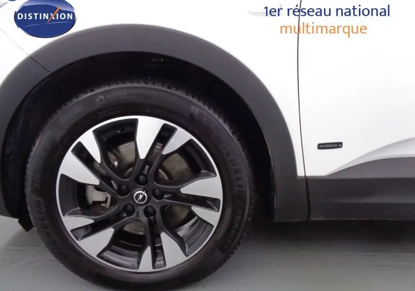Gros plan sur la roue avant gauche d'un Opel Grandland X blanc nacré avec jante alliage bicolore et badge Hybrid 4.