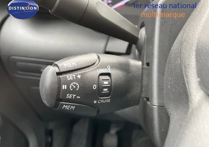 Gros plan sur la commande de régulateur de vitesse du Citroën C3 Aircross blanc polaire, version 2023, intérieur conducteur.