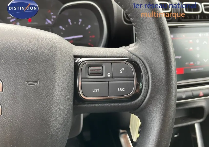 Gros plan sur les commandes au volant noir du Citroën C3 Aircross 2023, avec tableau de bord et écran tactile en arrière-plan.