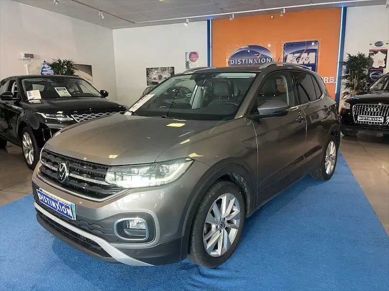 Volkswagen T-Cross gris Limestone métallisé vu de trois quarts avant droit en showroom avec éclairage intérieur.