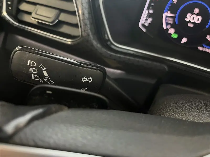 Gros plan sur le commodo de clignotants du Volkswagen T-Cross 1.0 TSI gris Limestone, avec tableau de bord numérique en arrière-plan.