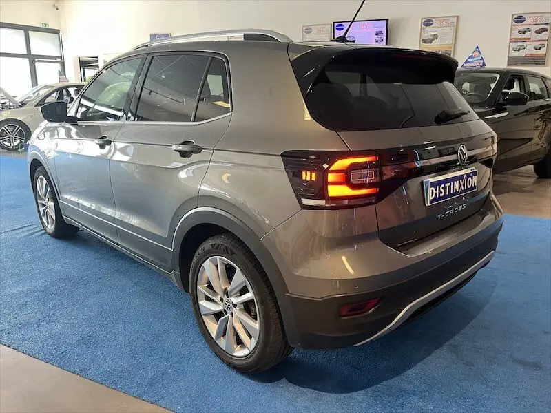 Vue 3/4 arrière droite d'un Volkswagen T-Cross gris Limestone métallisé avec feux arrière allumés en showroom.