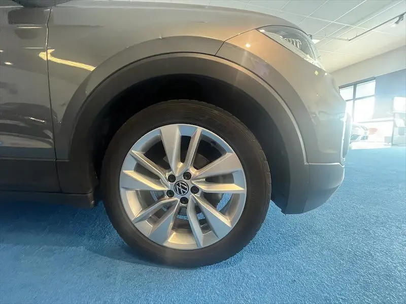 Gros plan sur la roue avant droite d’un Volkswagen T-Cross gris Limestone métallisé avec jante alliage en showroom.