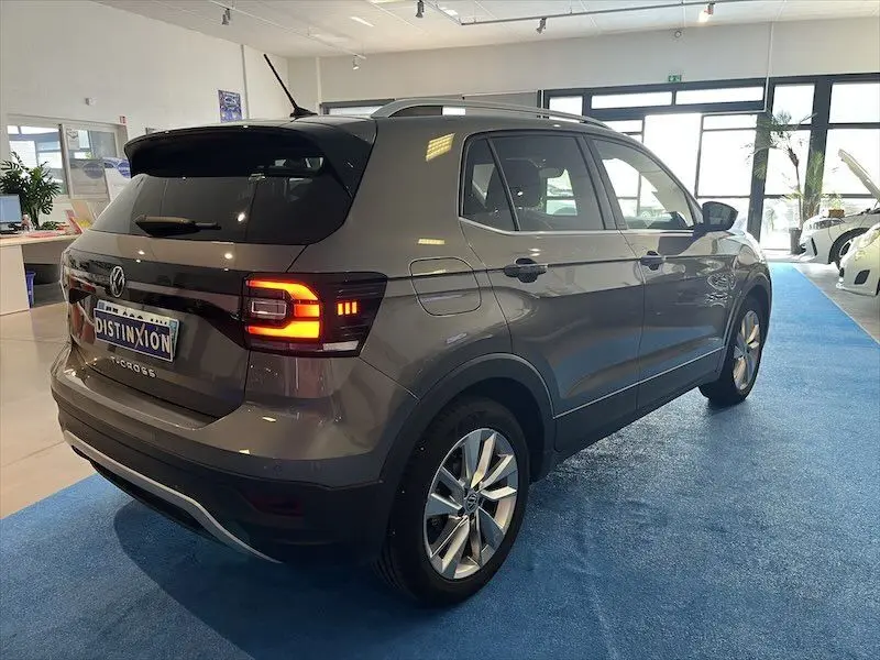 Volkswagen T-Cross gris Limestone métallisé vu de 3/4 arrière droit en showroom avec feux arrière allumés.