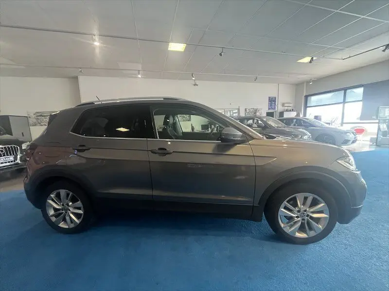 Profil côté droit du Volkswagen T-Cross gris Limestone métallisé 2021 en intérieur showroom avec jantes alliage visibles.
