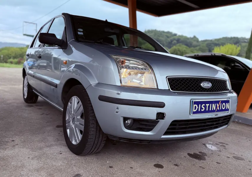 Ford Fusion bleu clair vue 3/4 avant droit avec rayures visibles sur le pare-chocs avant sous un abri.