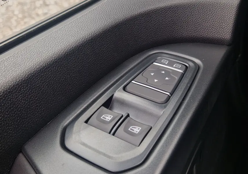 Boutons de commande des vitres et rétroviseurs électriques sur la porte côté conducteur du Renault Trafic Fourgon gris urbain 2025.