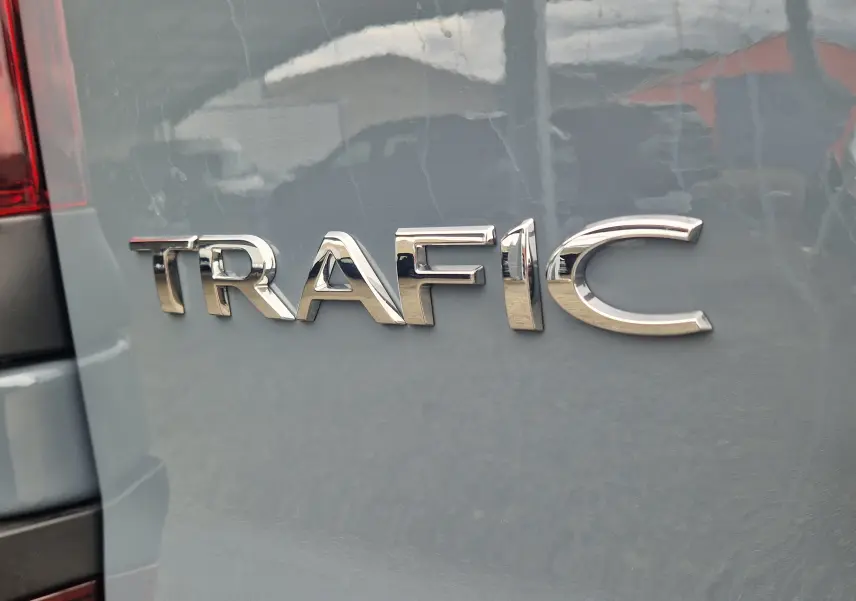 Gros plan sur l'arrière gris urbain du Renault Trafic avec l'inscription chromée "TRAFIC" visible sur la porte.