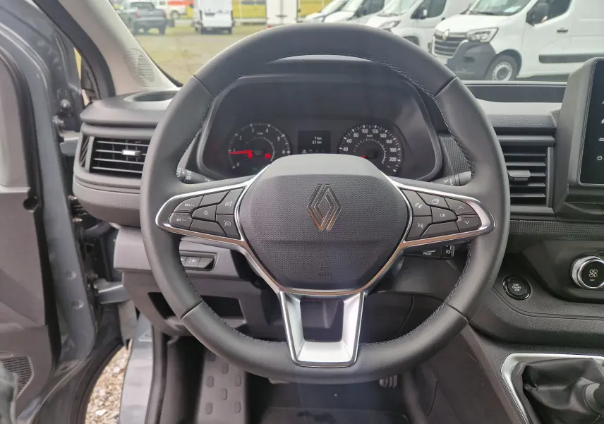 Vue intérieure centrée sur le volant noir du Renault Trafic Fourgon gris urbain, avec tableau de bord et commandes visibles.