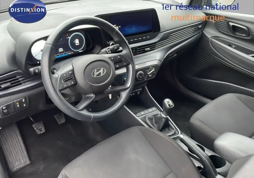 Vue intérieure côté conducteur de la Hyundai i20 2025 avec volant cuir, tableau de bord numérique et levier de vitesse manuel.