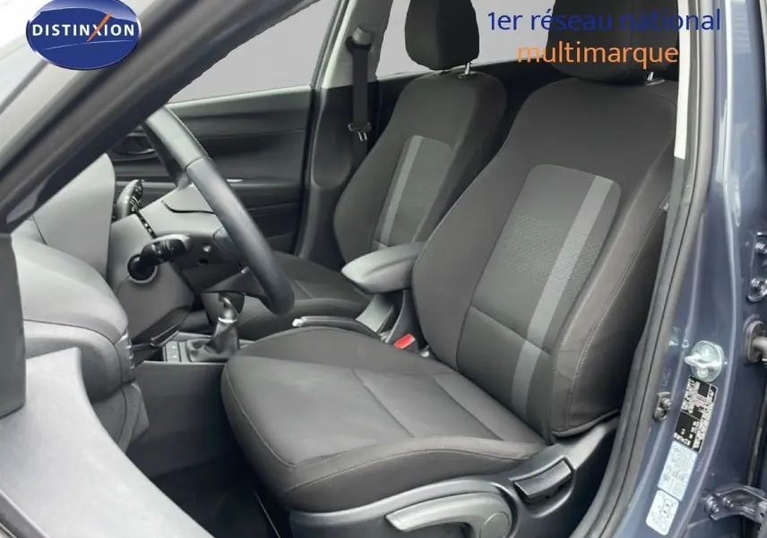 Vue intérieure côté conducteur de la Hyundai i20 gris Aurora Metal, montrant les sièges en tissu et cuir et le volant multifonction.