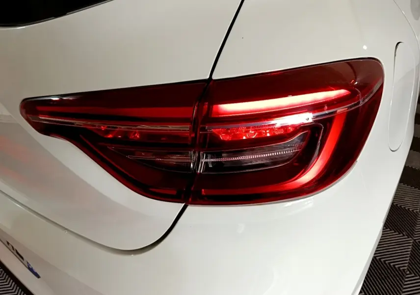 Gros plan sur le feu arrière droit rouge d’une Renault Clio Business blanche, vue de l’arrière côté droit.