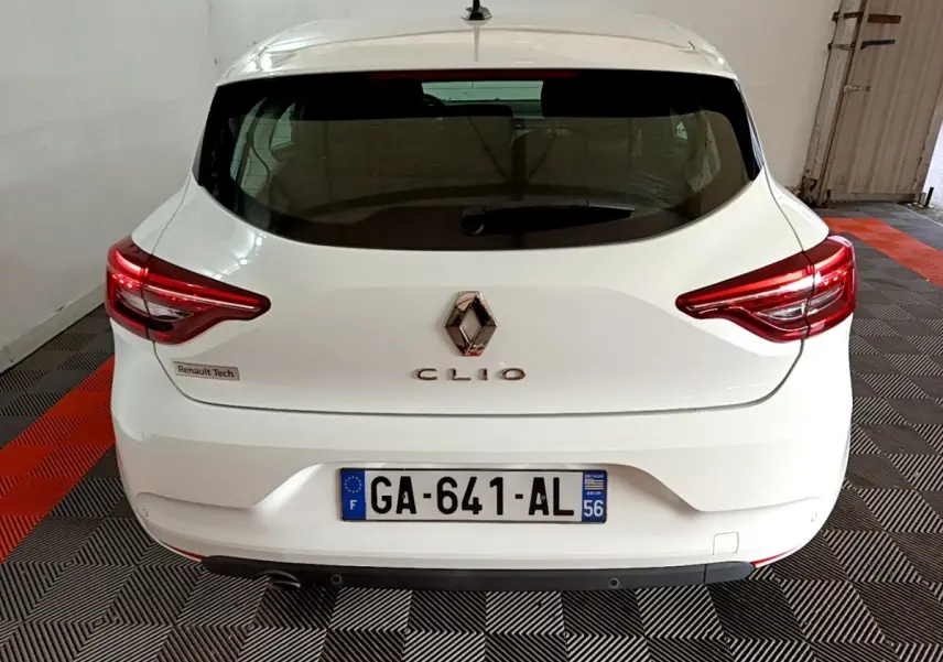 Vue arrière d'une Renault Clio blanche, avec feux arrière LED allumés et plaque d'immatriculation française visible.