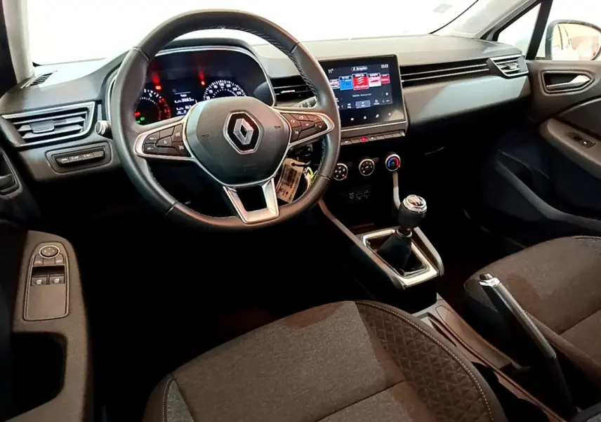 Vue intérieure avant droite de la Renault Clio Business blanche, volant cuir, écran tactile et boîte manuelle visible.