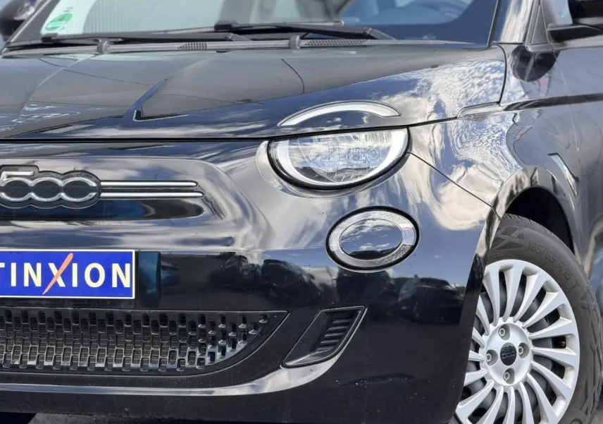 Gros plan 3/4 avant droit du Fiat 500 électrique 2024 en noir Onyx, mettant en valeur le phare rond et la calandre épurée.