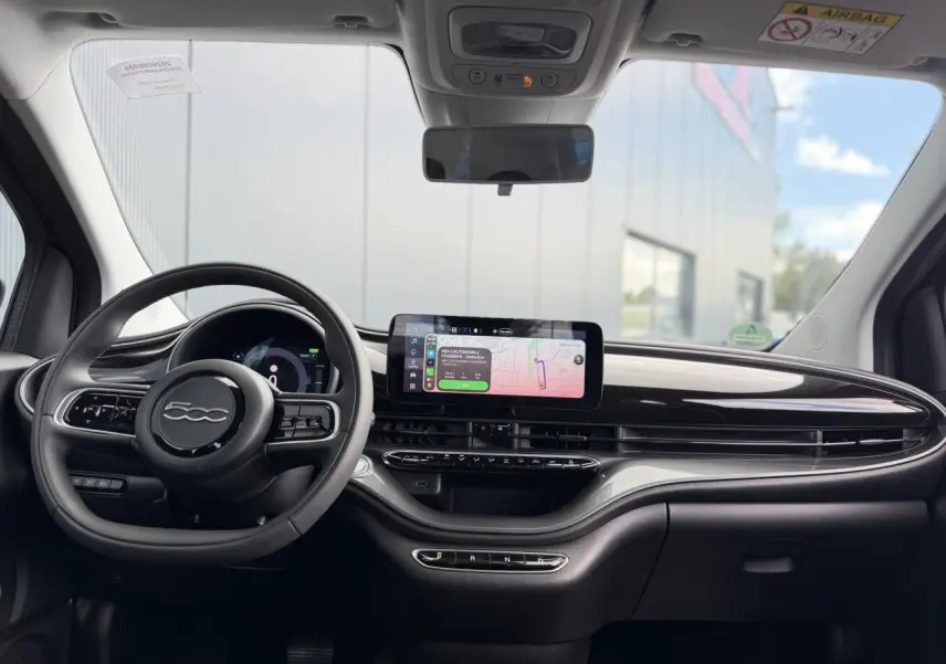 Vue frontale de l'habitacle du Fiat 500 électrique 2024, avec tableau de bord noir brillant et écran tactile central.