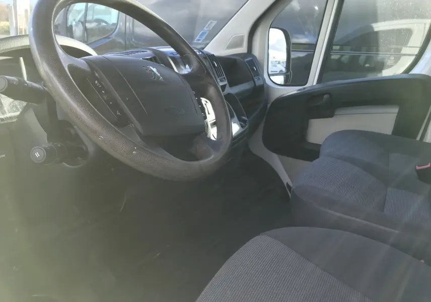 Vue intérieure côté conducteur du Peugeot Boxer Châssis Double Cabine blanc, montrant le volant et les sièges avant en tissu gris.