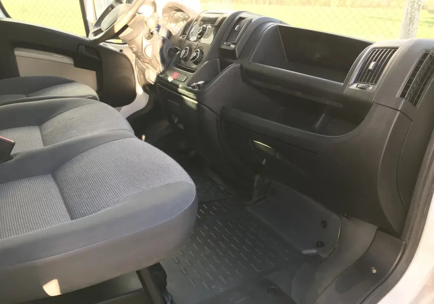 Intérieur côté passager du Peugeot Boxer blanc 2014, montrant les sièges gris et le tableau de bord noir avec commandes centrales.