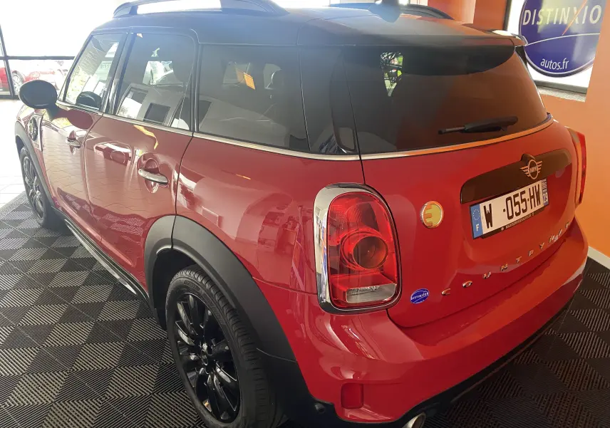 Vue 3/4 arrière droite d'une MINI Countryman rouge avec toit noir et jantes noires dans un showroom.