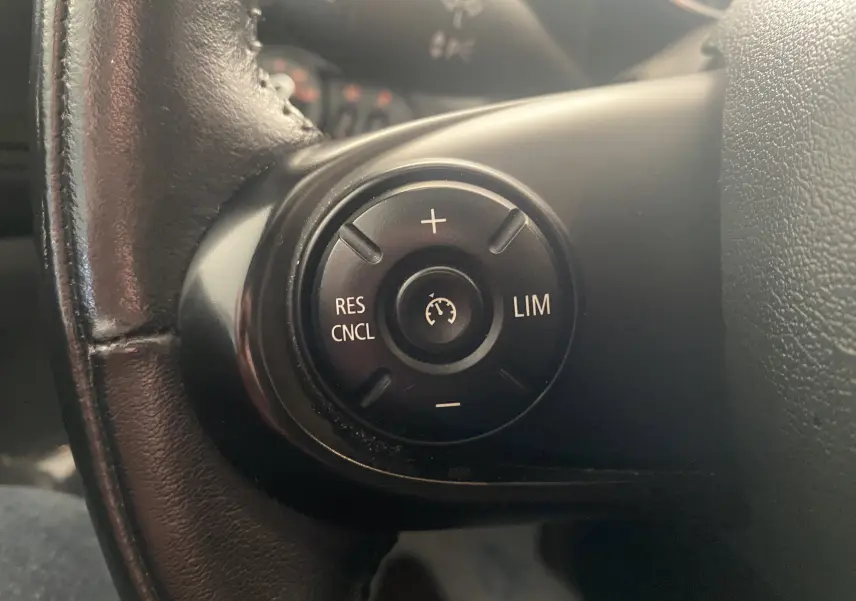 Gros plan sur les commandes de régulateur de vitesse au volant cuir noir d'une MINI Countryman rouge toit noir.