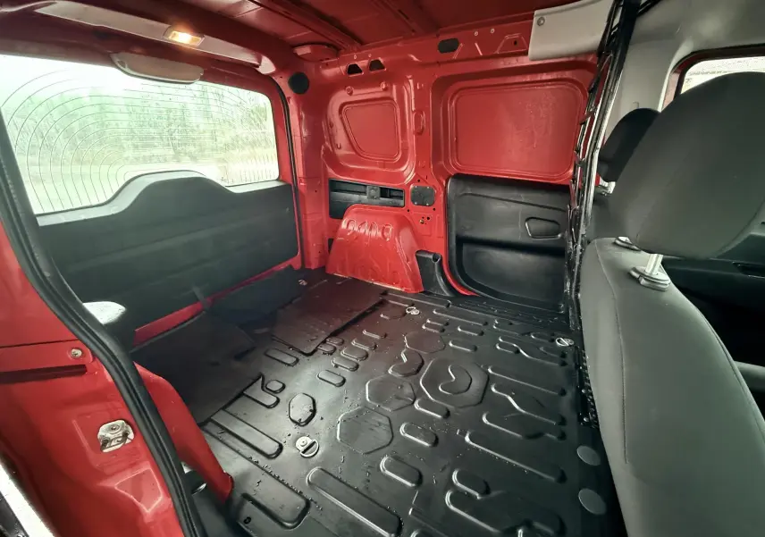 Vue intérieure arrière du Fiat Doblo Cargo rouge de 2011, montrant l'espace de chargement vide avec plancher en métal noir.