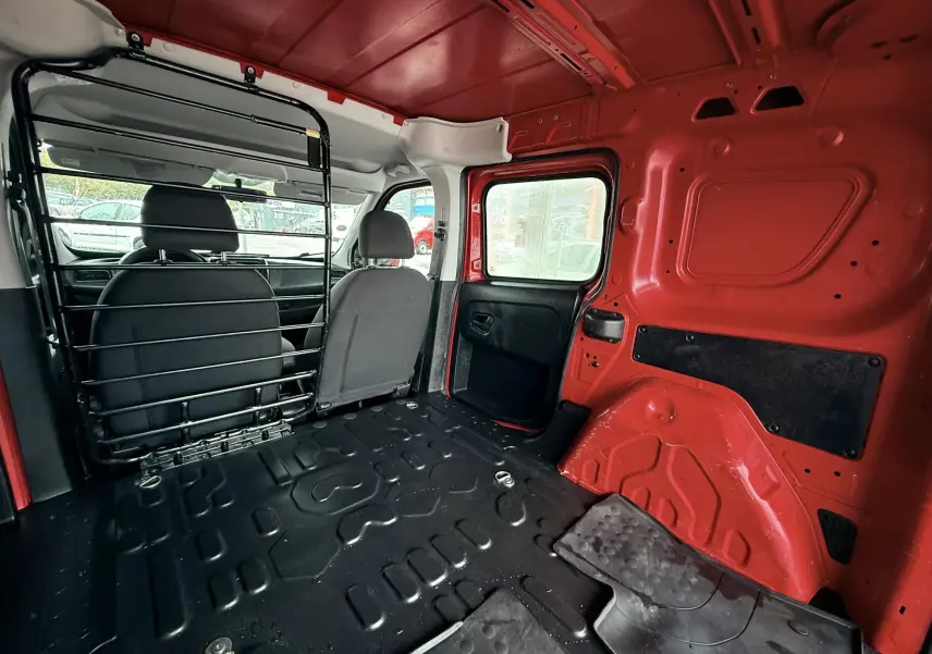 Vue intérieure arrière du Fiat Doblo Cargo rouge 2011, montrant l'espace de chargement et la séparation métallique avec les sièges avant.