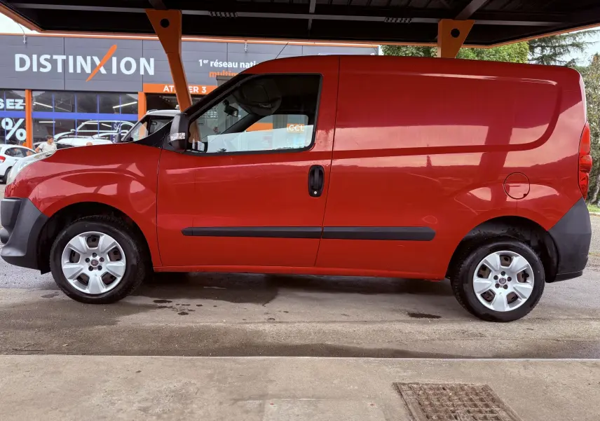 Vue latérale droite d’un FIAT Doblo Cargo rouge de 2011, utilitaire compact avec porte coulissante et jantes argentées.
