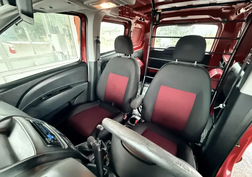 Vue intérieure avant du Fiat Doblo Cargo rouge de 2011, sièges tissu rouge et noir avec cloison métallique arrière.