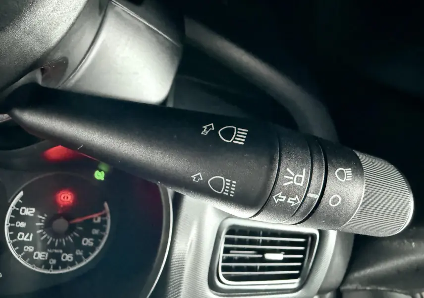 Gros plan sur la commande des phares et clignotants à gauche du volant dans un Fiat Doblo Cargo rouge.