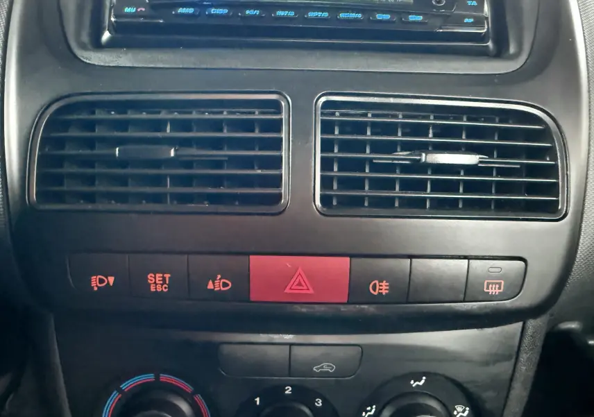 Vue rapprochée du tableau de bord noir du Fiat Doblo Cargo 2011, montrant les aérateurs centraux et les commandes de climatisation.