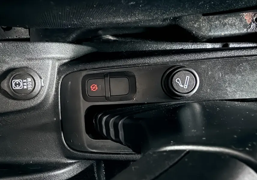 Gros plan sur la console centrale noire du Fiat Doblo Cargo 2011, montrant les boutons de commande et prise 12V.