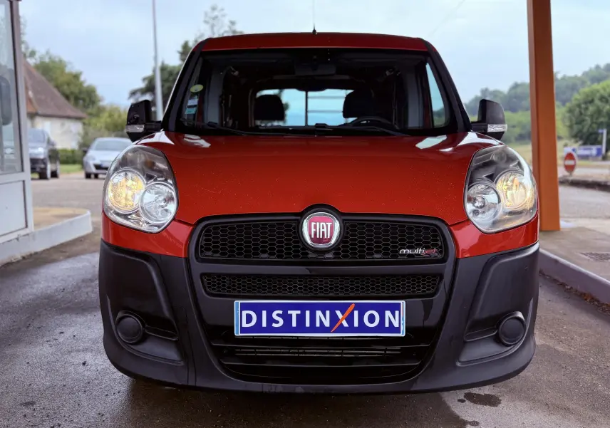 Vue frontale d’un FIAT Doblo Cargo rouge avec phares allumés et calandre noire, plaque Distinxion visible.
