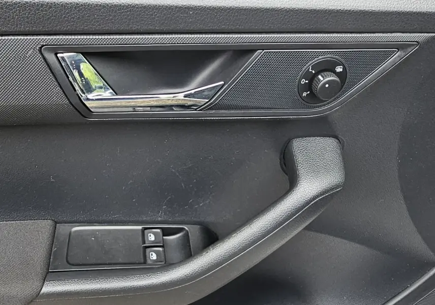 Gros plan sur la porte avant gauche d'une Skoda Fabia blanche, montrant la poignée, les commandes de vitres et le réglage des rétroviseurs.