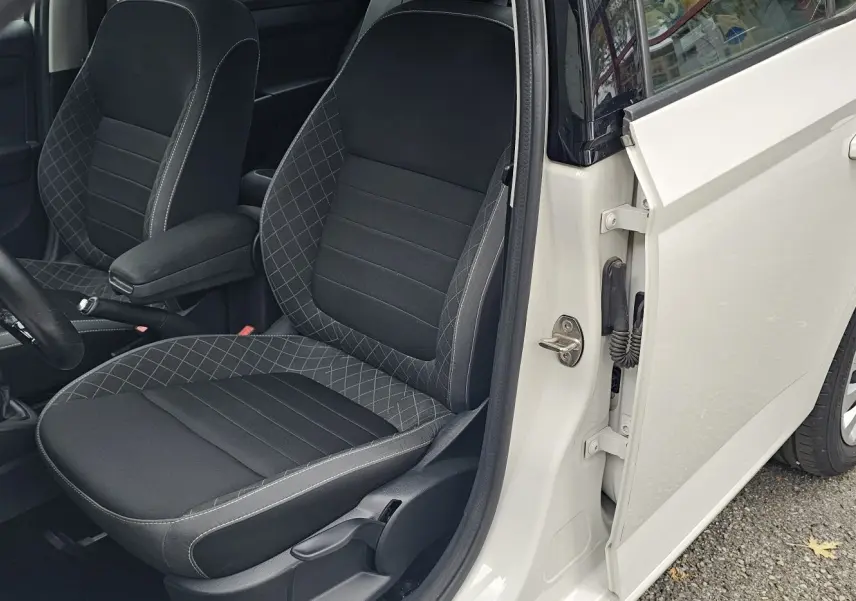 Vue intérieure côté conducteur d'une Skoda Fabia blanche cristal, mettant en valeur la sellerie Business noire satin avec surpiqûres grises.