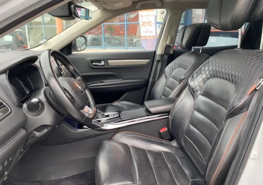 Intérieur du Renault Koleos blanc 2019, vue côté conducteur, sièges cuir noir avec surpiqûres orange et tableau de bord moderne.