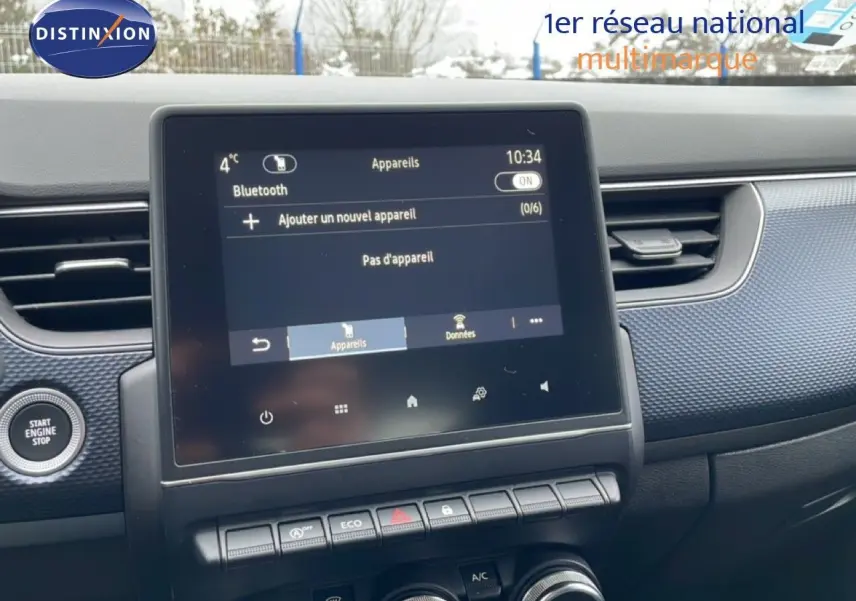 Vue rapprochée de l’écran tactile central et tableau de bord du Renault Arkana bleu Zanzibar, avec commandes climatisation et démarrage.