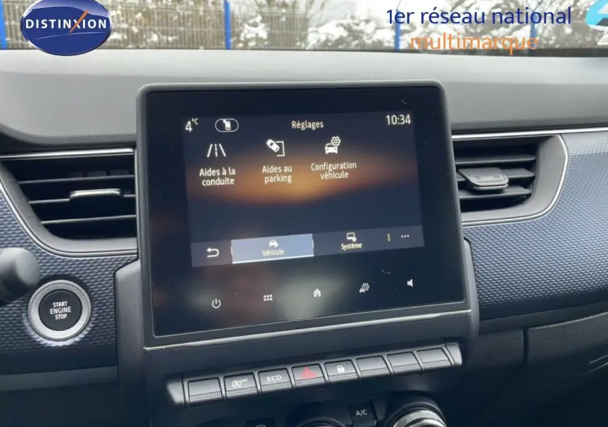 Vue intérieure centrée sur l’écran tactile et la console d’une Renault Arkana 1.3 Mild Hybrid bleu Zanzibar, avec bouton start visible.