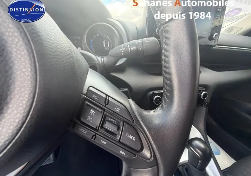 Vue rapprochée du volant de la Toyota Yaris Hybrid 2023, montrant les commandes intégrées et la console de boîte automatique.