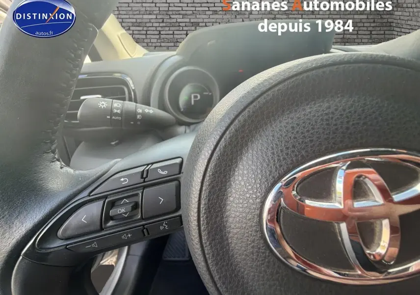 Gros plan sur le volant noir de la Toyota Yaris Hybrid 2023, mettant en valeur les commandes intégrées et le logo chromé.