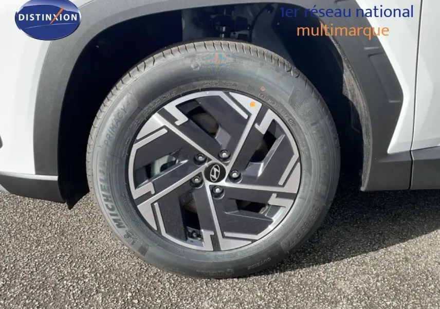 Gros plan sur la roue avant gauche du Hyundai Tucson blanc Atlas avec jante alliage noire et grise au design géométrique.