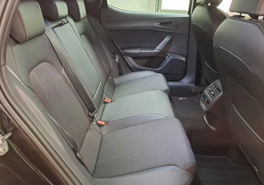 Vue latérale gauche de l'intérieur arrière du CUPRA Leon 2025 noir minuit avec sièges en tissu et cuir noir.