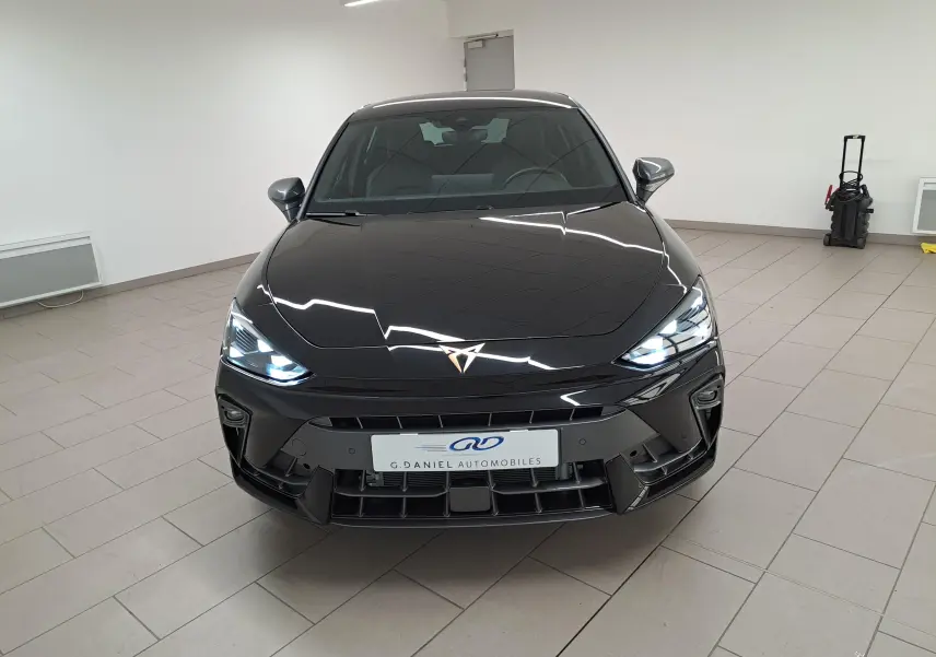 Vue avant d'une CUPRA Leon Ph.2 2025 en Noir Minuit avec phares allumés et logo cuivré distinctif.