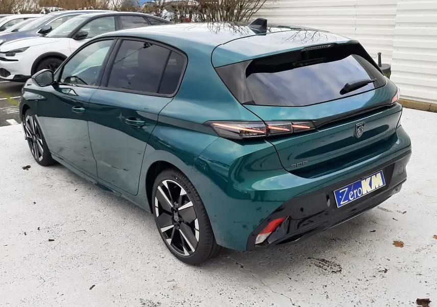 Vue 3/4 arrière droite d'une Peugeot 308 1.2 Hybrid GT 2026 en bleu Lagoa avec jantes noires bicolores et vitres teintées.
