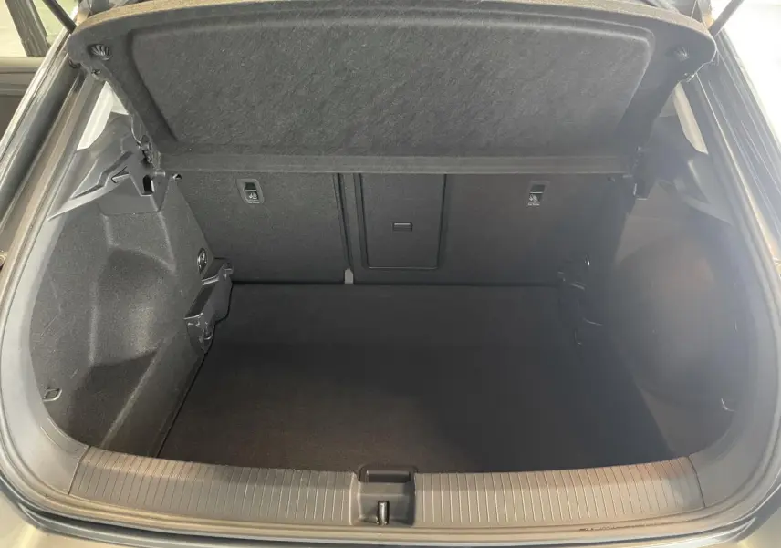 Coffre ouvert vu de l'arrière d'un Volkswagen T-Roc 2025 gris Indium, intérieur noir et moquette propre.