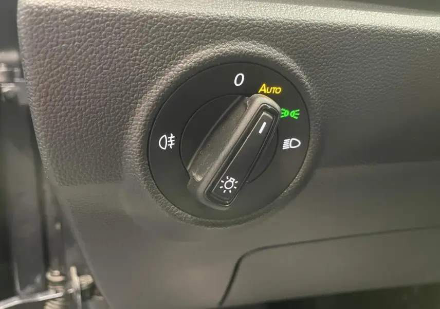 Gros plan sur le bouton de commande des phares du Volkswagen T-Roc, tableau de bord noir texturé.